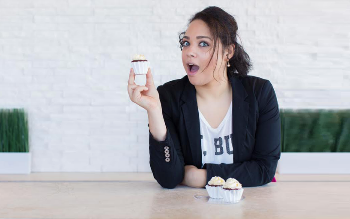 Ashley-Victoria Smith seated at a table making a suprised face with a cupcake