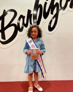 Farrah posing in front of a Barbizon sign wearing her winning sash