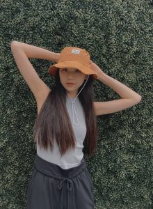 Lily in front of a green planted background modeling with an orange bucket hat on