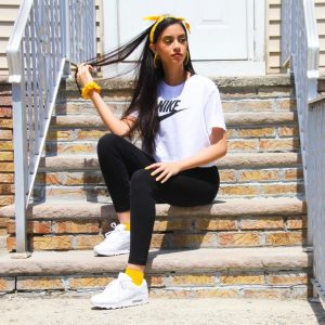 Alana seated on a porch stoop wearing athletic clothes and large yellow hoop earrings