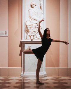 Alana in a dancer's pose in front of a statue at a museum