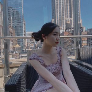 Lily seated on a rooftop against a NYC skyscape