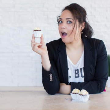 Ashley-Victoria Smith seated at a table making a suprised face with a cupcake