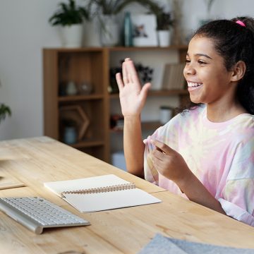 Young Girl sitting at a computer waving and smiling at the screen