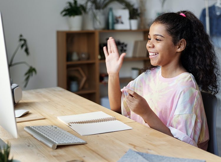 Young Girl sitting at a computer waving and smiling at the screen